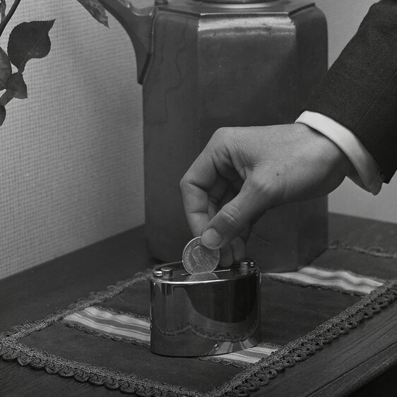 Nicht nur zuhause wurden Herr und Frau Schweizer zum Sparen motiviert. Ein Mann legt einen Fünfliber in ein Sparkässeli, 1963. Comet Photo AG.