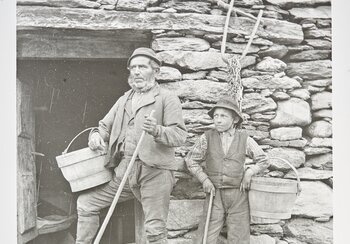 Die Alpwirtschaft verhilft auch Kleinbauern zu Überleben. Der Senn melkt die Kühe von Hand. Unterstützt wird er von einem Hirtenjungen, der das Vieh auch hütet. Neben langen Arbeitstagen sind diese Kinder in der Abgeschiedenheit der Alp den Launen des Senns ausgeliefert. Senn und Knabe, 1890 - 1930, Tessiner Alp, Foto Rudolf Zinggeler-Danioth, Kilchberg, Schweizerisches Nationalmuseum