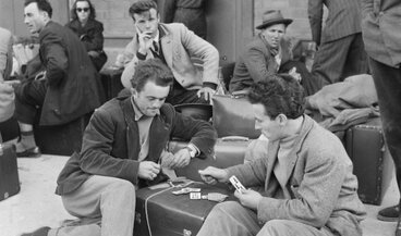 Historical photograph of migrants waiting with luggage at the train station.