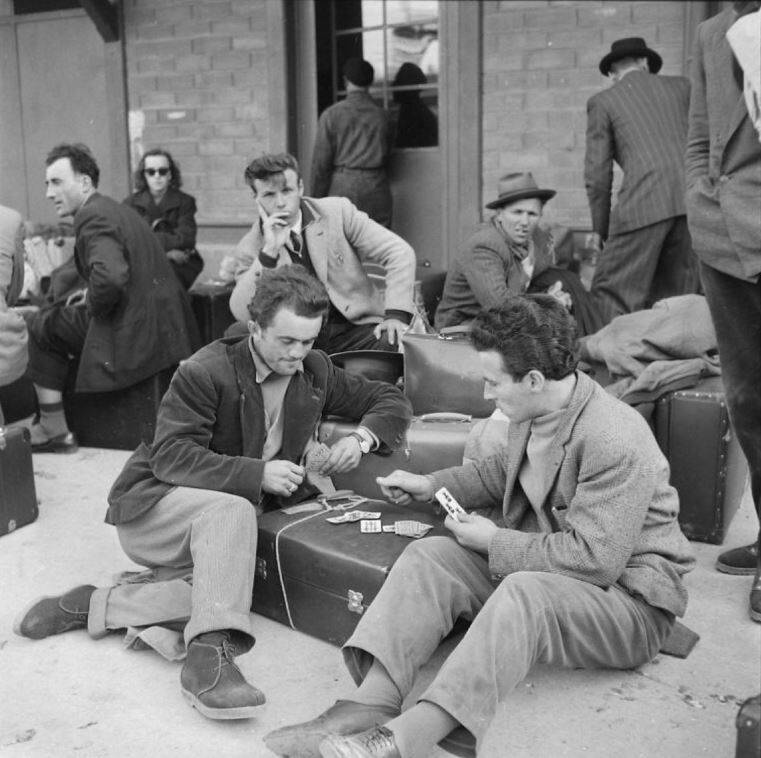 Photographie historique de migrants attendant à la gare avec leurs bagages.