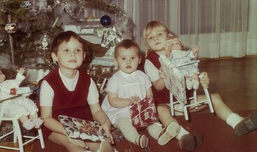 Drei Kinder sitzen unter dem geschmückten Christbaum.