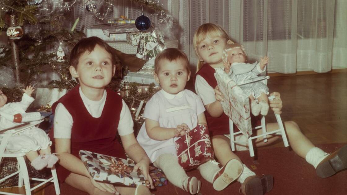 Drei Kinder sitzen unter dem geschmückten Christbaum.