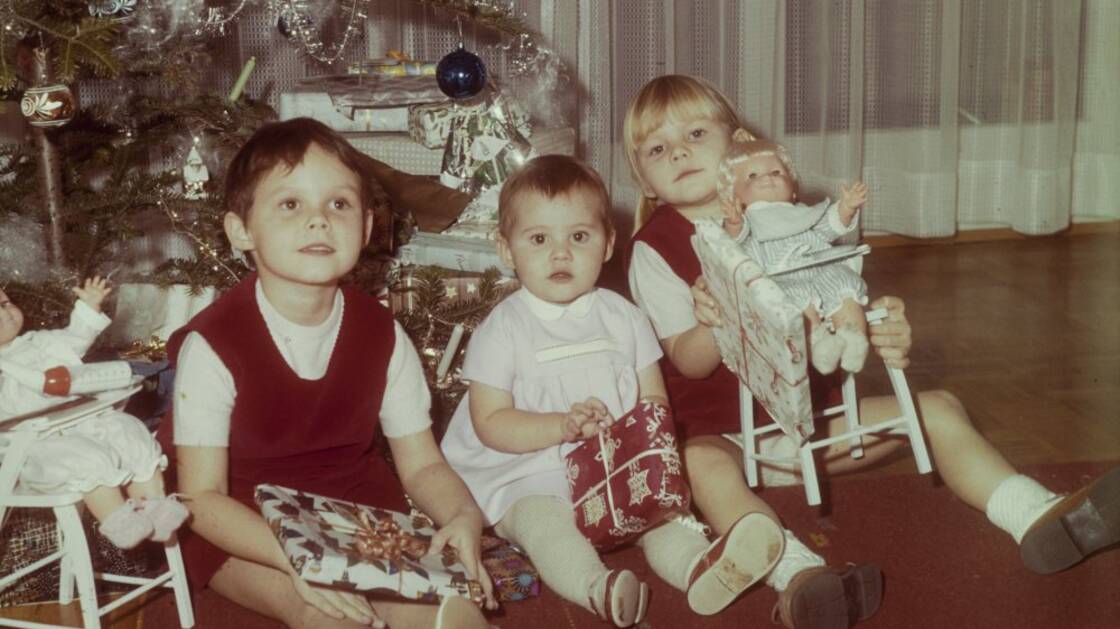 Tre bambini siedono sotto l'albero di Natale decorato.