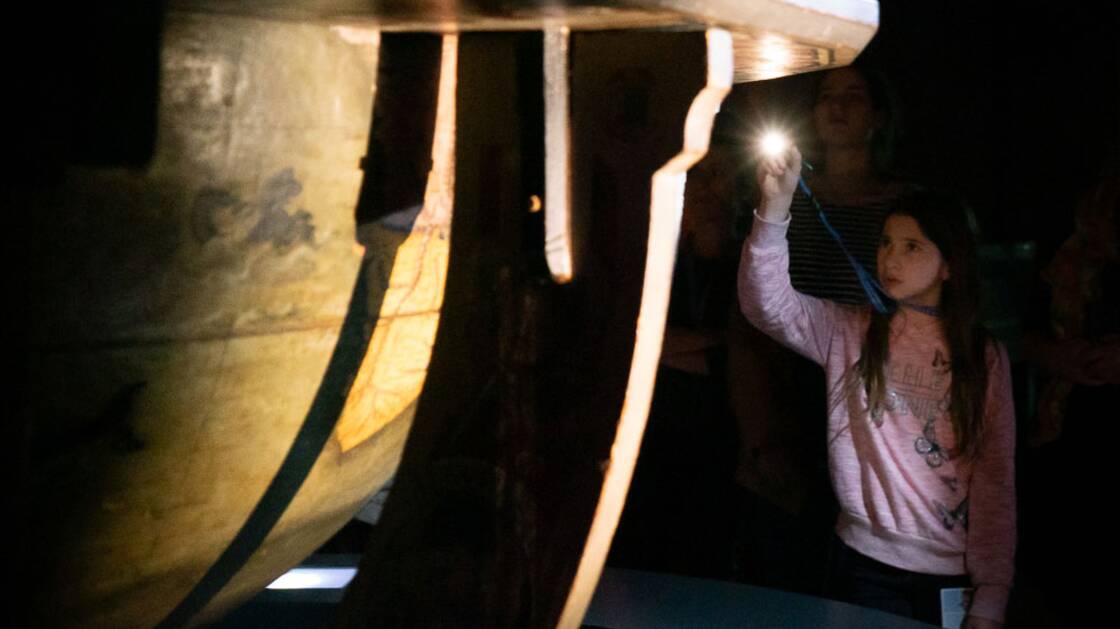 A girl explores an object with a torch during the guided tour "Alone at night in the museum".