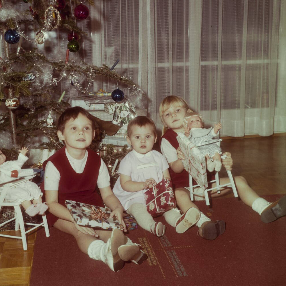 Drei Kinder sitzen unter dem geschmückten Christbaum.