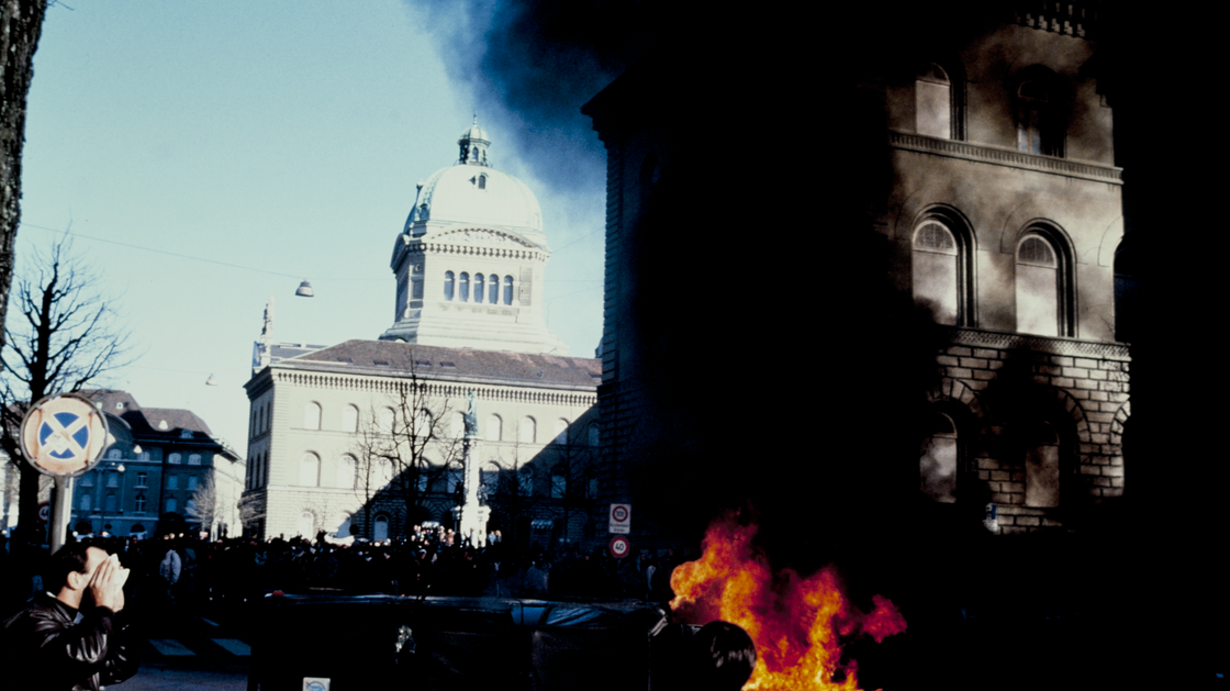 Feu et fumée lors de la manifestation contre le fichage par l'Etat de personnes politiquement suspectes, avec le Palais fédéral en arrière-plan